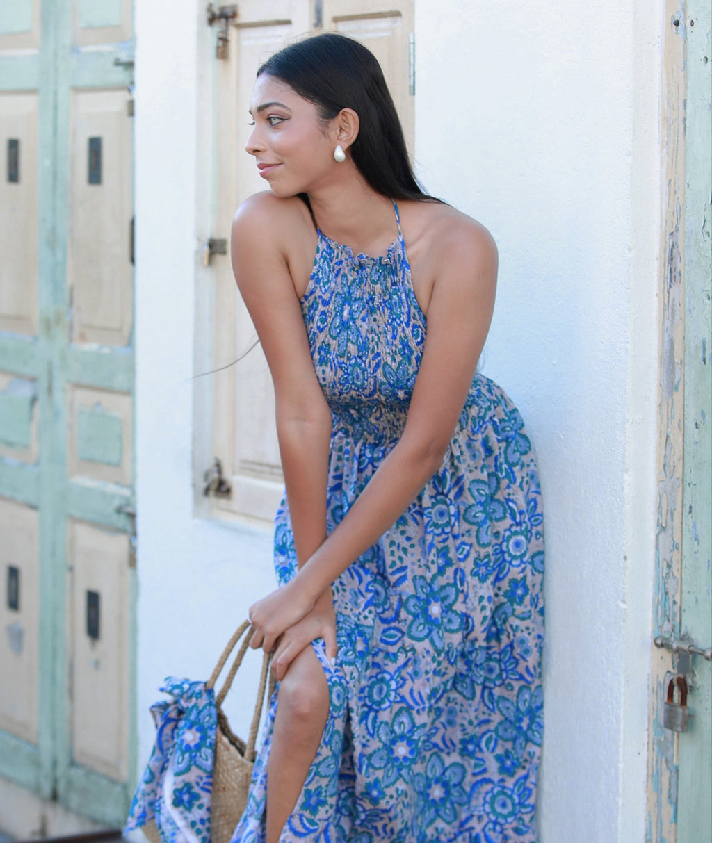 Woman in a blue floral dress standing in front of a white wall with green doors.