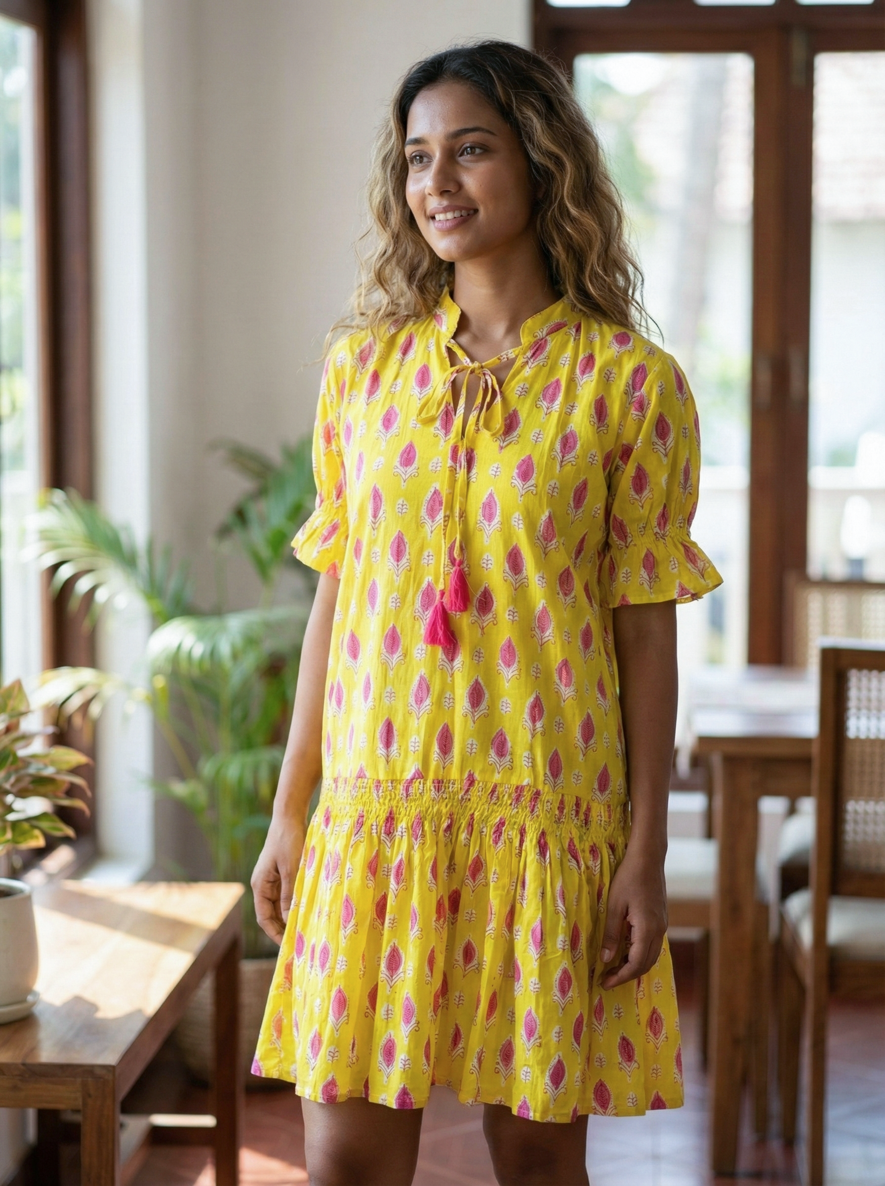 Woman wearing a yellow dress with pink floral pattern indoors